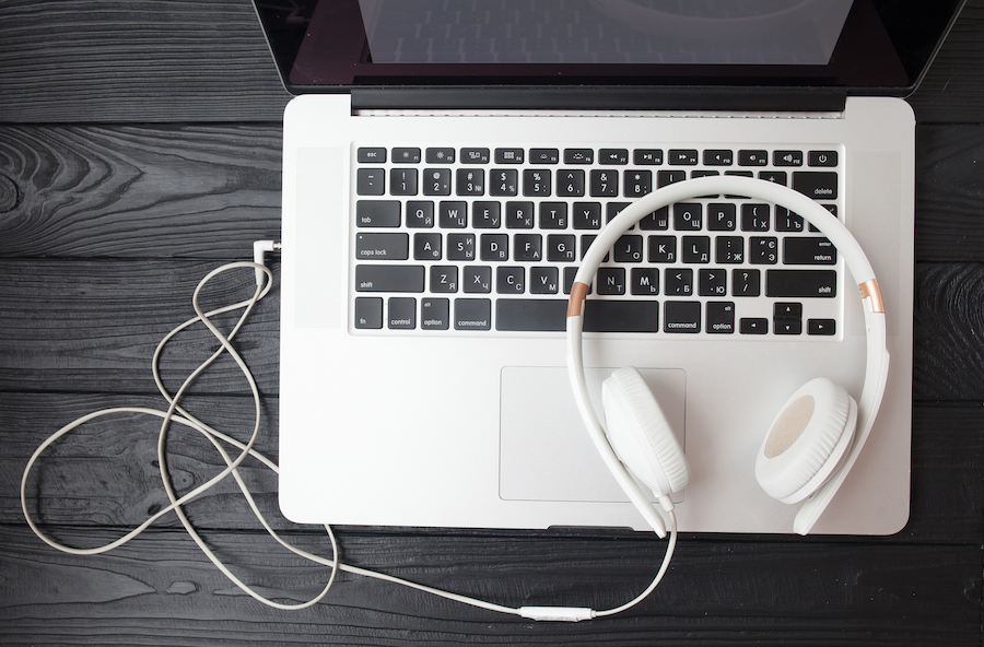 laptop on a table with a pair of white headphones plugged in and sitting on top